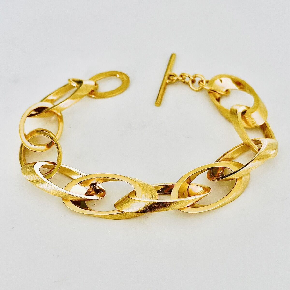 Ein feingoldplattiertes Silberarmband mit stilvollen Kettengliedern vor weißem Hintergrund.