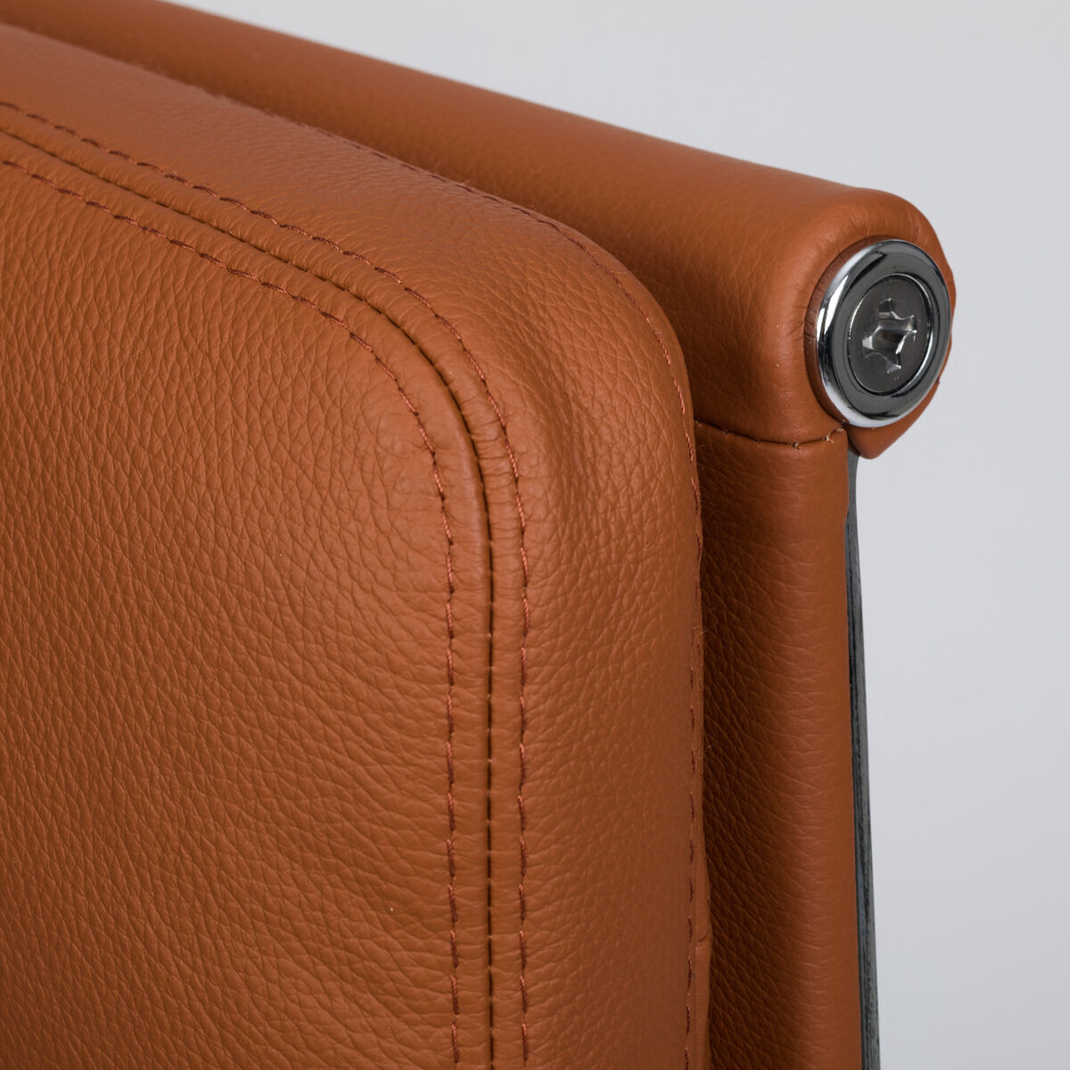 Detailaufnahme der Rückseite eines Vitra Soft Pad EA219 Schreibtischstuhls in cognacfarbenem Leder, sichtbar ist die hochwertige, weich gepolsterte Lederoberfläche mit feiner Narbung und exakten Doppelnähten, Metallapplikation an der Kante, moderner Designklassiker.