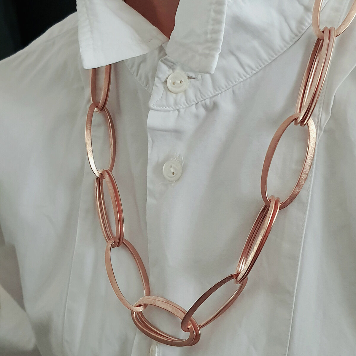Eine Person trägt das roségoldplattierte Collier »GRACE« von HML Berlin. Die Kette besteht aus ovalen, größeren Gliedern in edler Roségoldoptik und liegt auf einer weißen Bluse. Das Design wirkt modern, elegant und puristisch.