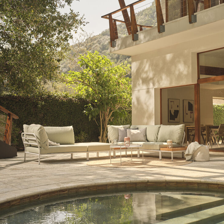 Ein modernes Ecksofa der Lounge-Serie »LEVEL 2« steht auf einer Terrasse neben einem Pool, umgeben von Natur mit Bäumen und einem Holzbalkon im Hintergrund. Die Polster des Sofas sind hell, passend zur entspannten Atmosphäre.