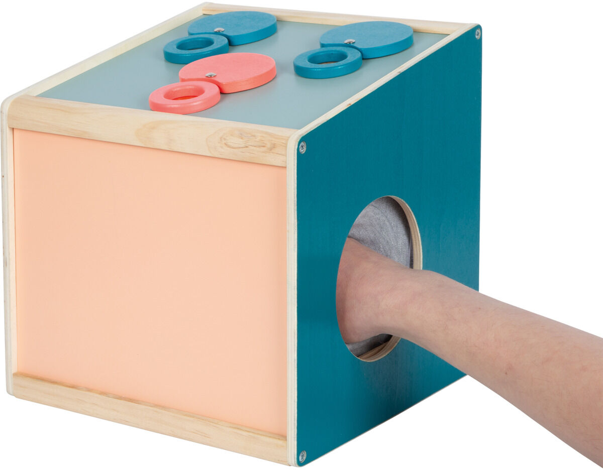 Ein Sinnes- und Fühlbox-Spielzeug aus Holz mit verschiedenen Farben, das über runde Öffnungen verfügt, um sensorische Erfahrungen zu ermöglichen. Eine Person steckt die Hand durch eine Öffnung. Das Design ist schlicht und ansprechend für Kinder.