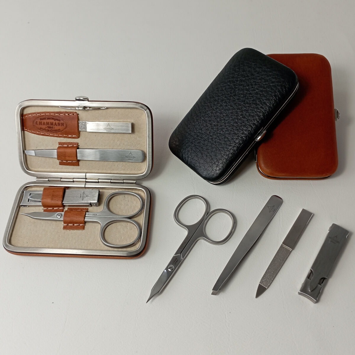 Ein Maniküre-Set besteht aus verschiedenen Werkzeugen zur Nagelpflege, wie Schere, Feile, Pinzette und Nagelknipser, ordentlich in einem schwarzen und braunen Lederetui arrangiert.
