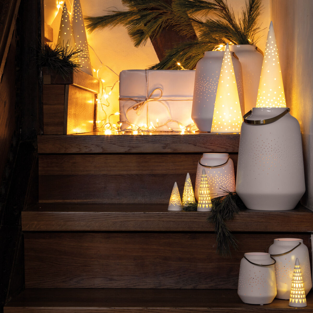 Eine stimmungsvolle Szene von einer Treppe, die mit Porzellanlaternen und warmweiß leuchtenden LED-Lichtern dekoriert ist. Im Hintergrund sind Geschenke und Tannenzweige zu sehen, was eine weihnachtliche Atmosphäre schafft.