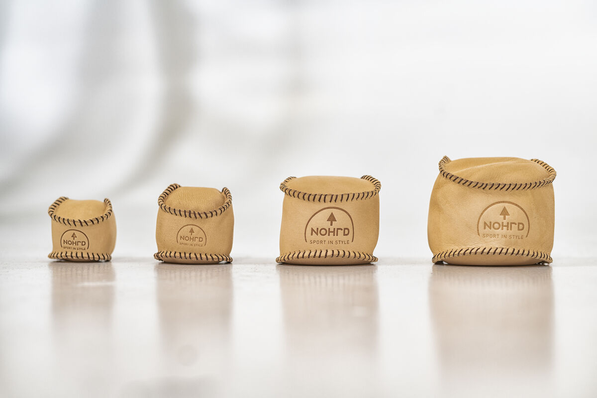 Vier HaptikBälle aus Holz in verschiedenen Größen, aufgereiht auf einem hellen Untergrund. Die Bälle haben eine glatte, natürliche Oberfläche mit einer dekorativen, dunklen Umrandung.