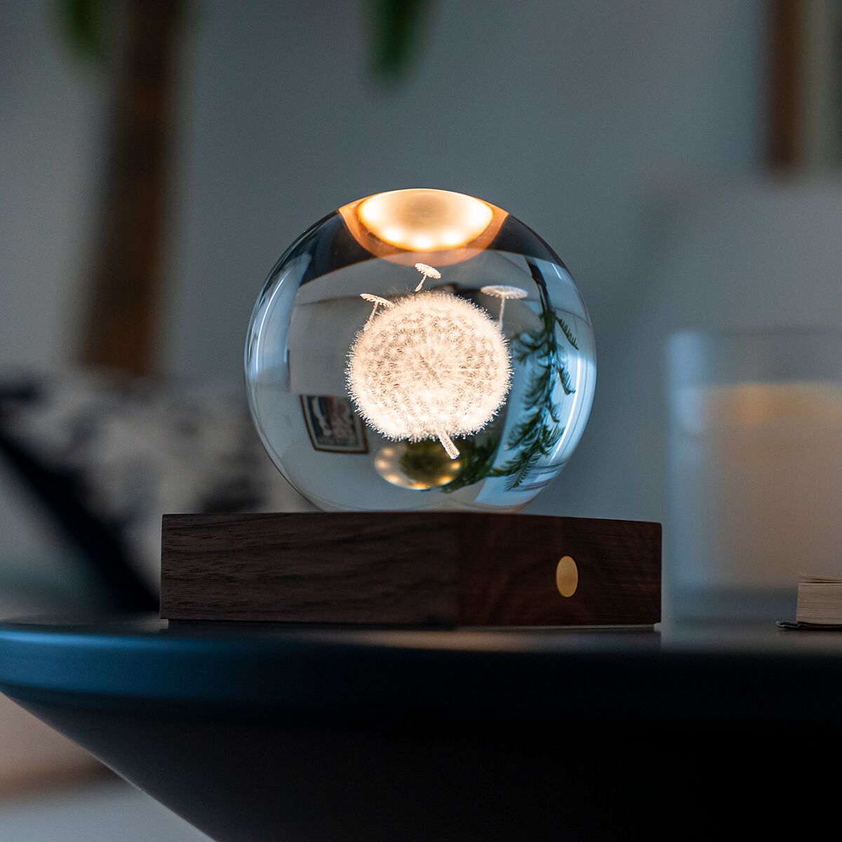 Eine elegante Tischlampe von Gingko Design mit einem runden Sockel aus dunklem Walnussholz und einer transparenten Kristallglaskugel. Im Inneren der Kugel ist eine filigrane 3D-Pusteblumen-Gravur, die von warmem Licht beleuchtet wird.