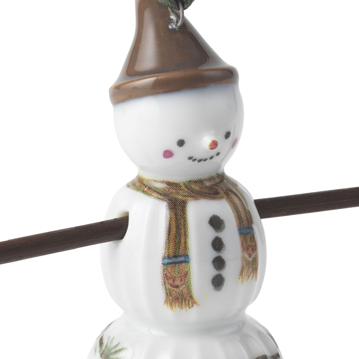 Porzellan-Anhänger in Form eines Schneejungen mit brauner Mütze, bunter Schal und bemalten Knöpfen. Der Anhänger hält einen braunen Stock und ist mit Tannenzweig- und Zuckerstangen-Motiv verziert. Geeignet als Weihnachts- oder Winterdeko, besonders für Familien und Kinder.