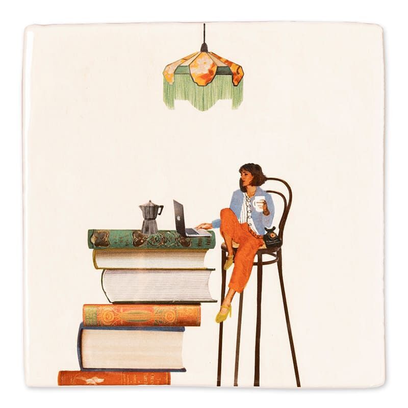Quadratische Keramikfliese mit Illustration einer Frau, die auf einem hohen Stuhl sitzt, eine Tasse Kaffee hält und an einem Laptop arbeitet. Sie sitzt neben einem großen Stapel bunter Bücher unter einer grünen Lampe. Das Design wirkt gemütlich und inspiriert zur Entspannung und Produktivität.