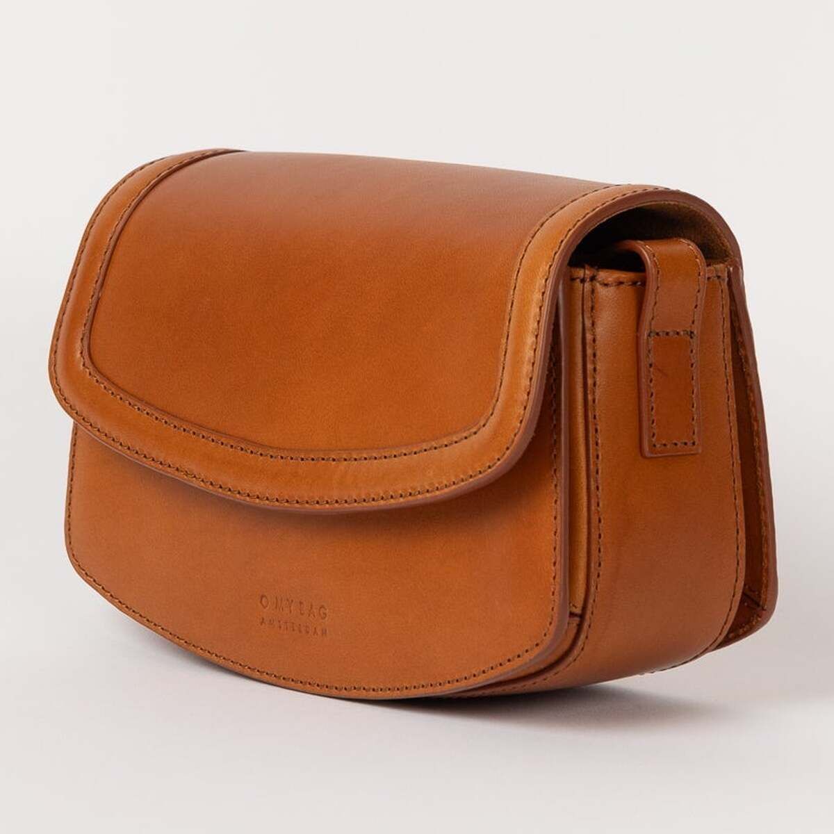 Eine kleine, stilvolle Umhängetasche aus glattem braunem Leder mit abgerundeten Ecken und Klappverschluss vor neutralem, hellem Hintergrund.