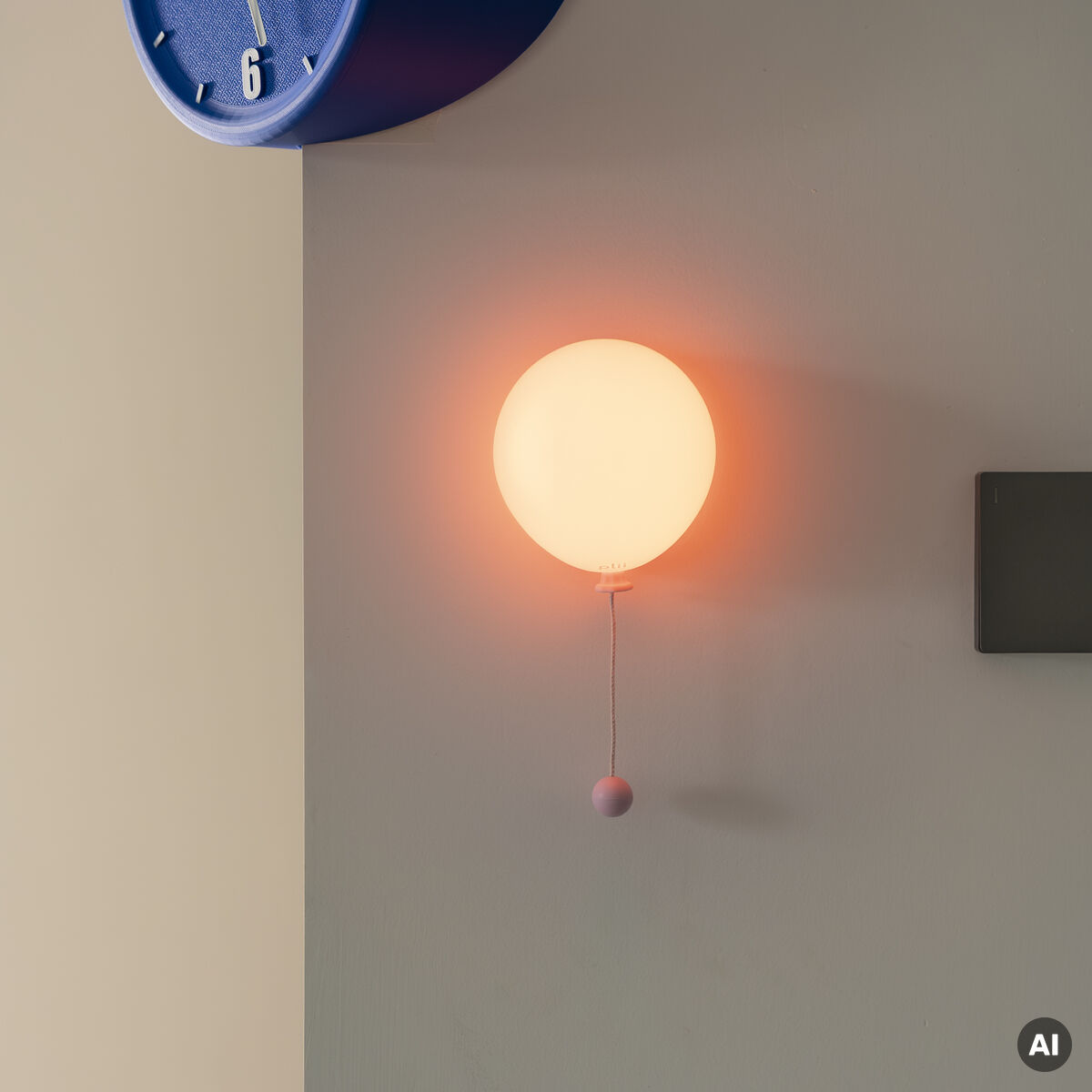 An einer grauen Wand hängt die runde Leuchte »Mimo Ballon« von Gingko Design Ltd in der Farbe blush bloom. Sie leuchtet warm orange und wirkt wie ein schwebender Ballon mit Zugband. Darüber ist eine blaue Wanduhr zu sehen. Klare, moderne Raumgestaltung.