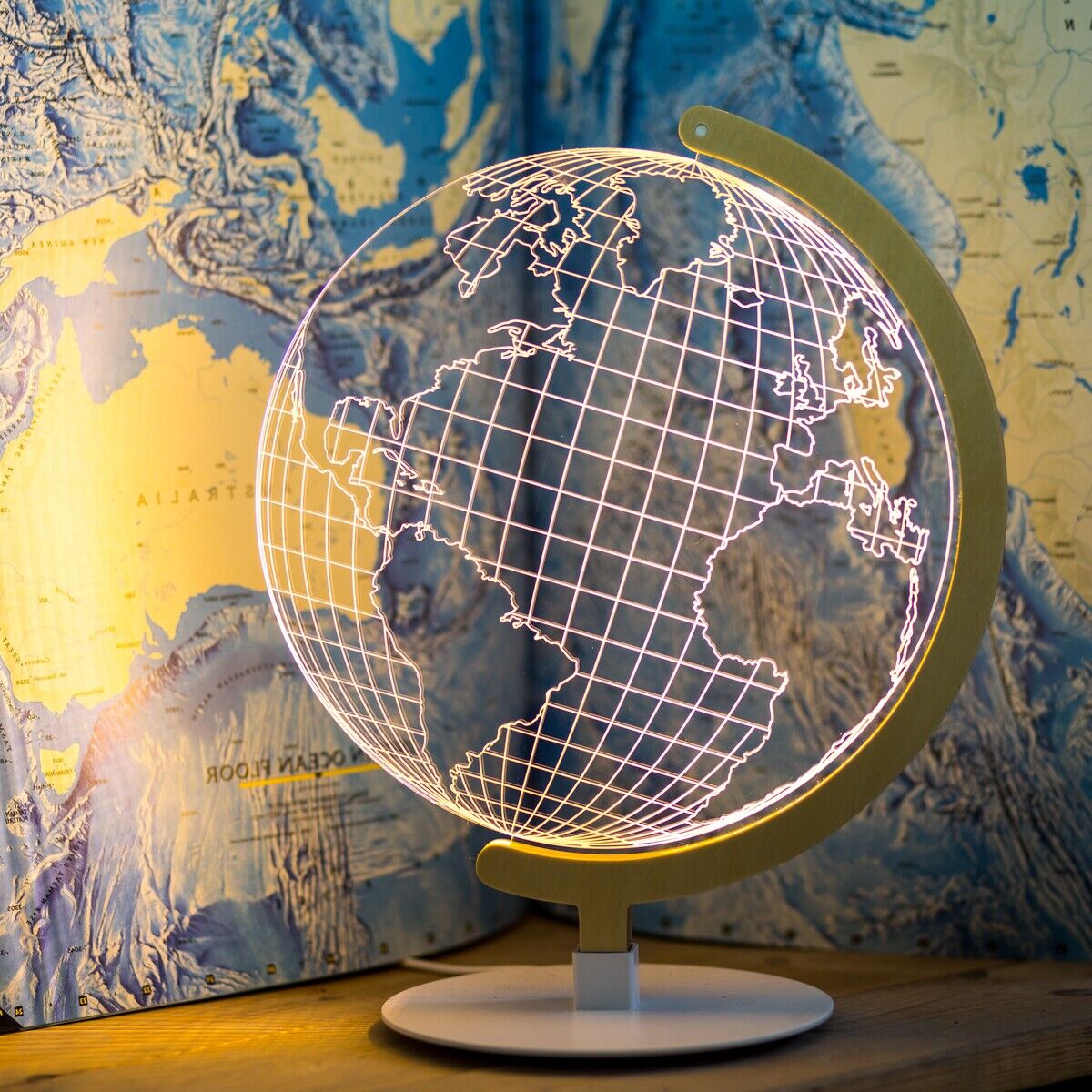 Eine LED-Leuchte in Form eines Globus vor einer detaillierten Weltkarte. Das Licht erzeugt einen 3D-Effekt und zeigt die Kontinente und die weltweiten Längengrade und Breitengrade.