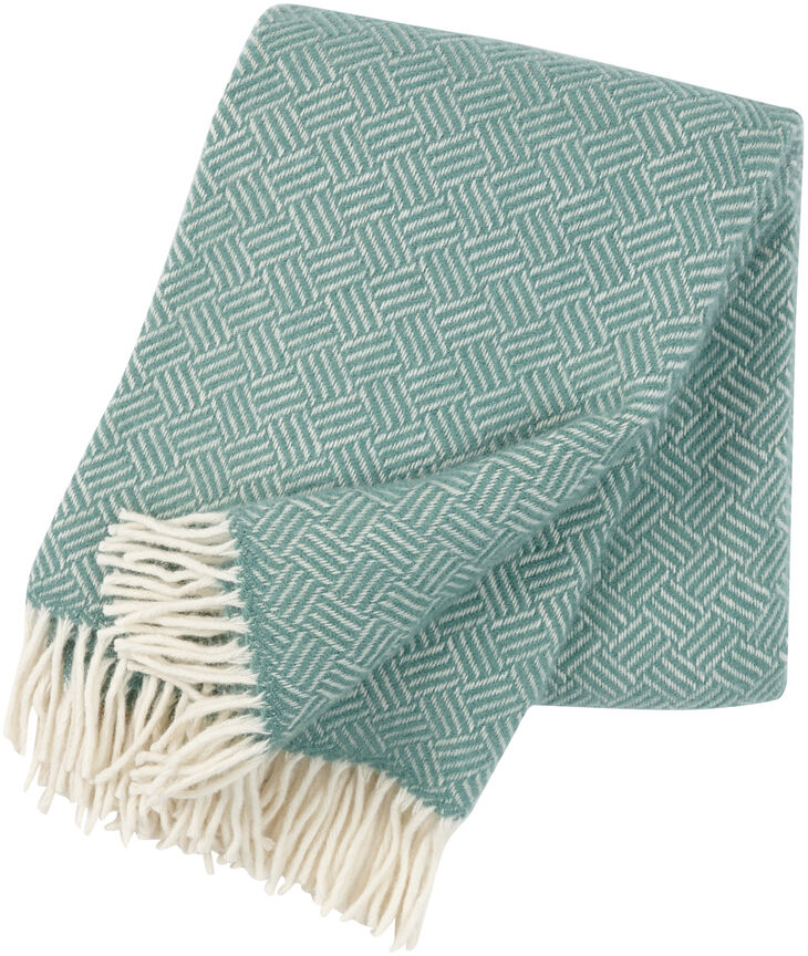 Eine grüne Decke mit einem geometrischen Muster und weißen Fransen, genannt »Samba«, perfekt für gemütliche Abende.