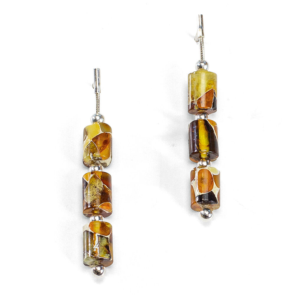 Das Bild zeigt ein Paar lange Ohrhänger aus dem Bernstein-Schmuckset 'Jantara' der Marke Ars mundi. Die Ohrhänger bestehen aus drei facettierten, zylinderförmigen Bernsteinen in unterschiedlichen goldbraunen und honigfarbenen Tönen, gefasst in 925er-Sterlingsilber.
