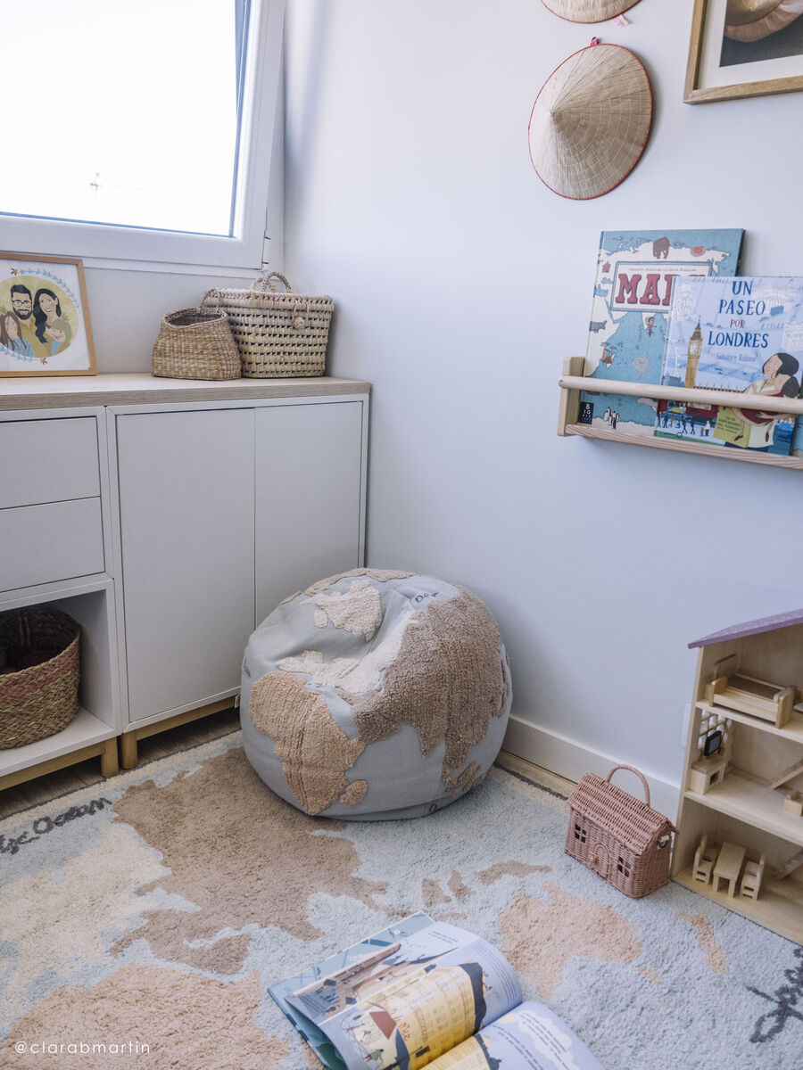 Ein Sitzkissen in Form eines Poufs mit Weltkartenmotiven, platziert in einem hellen und modernen Kinderzimmer. Das Zimmer ist mit Körben, Regalen und kindgerechten Büchern dekoriert.