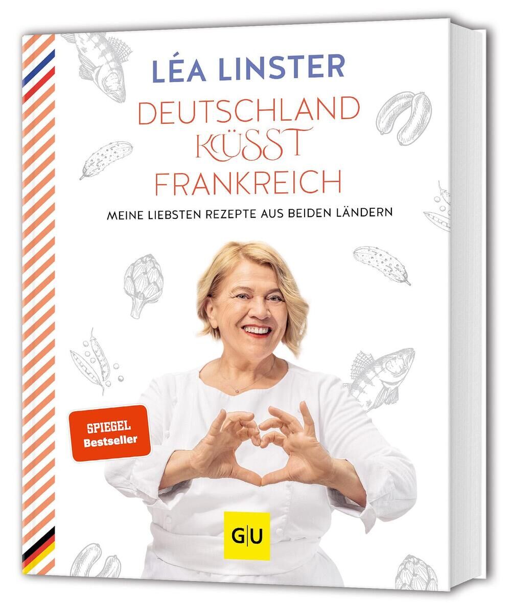 Das Buchcover von 'Deutschland küsst Frankreich' von Léa Linster zeigt die Autorin in einem weißen Oberteil lächelnd und mit den Händen ein Herz formend. Der Titel ist in roter und schwarzer Schrift gehalten, daneben sind illustrierte Lebensmittel wie Croissants und Krabben zu sehen. Am rechten Rand sind die Farben der deutschen und französischen Flaggen zu erkennen.