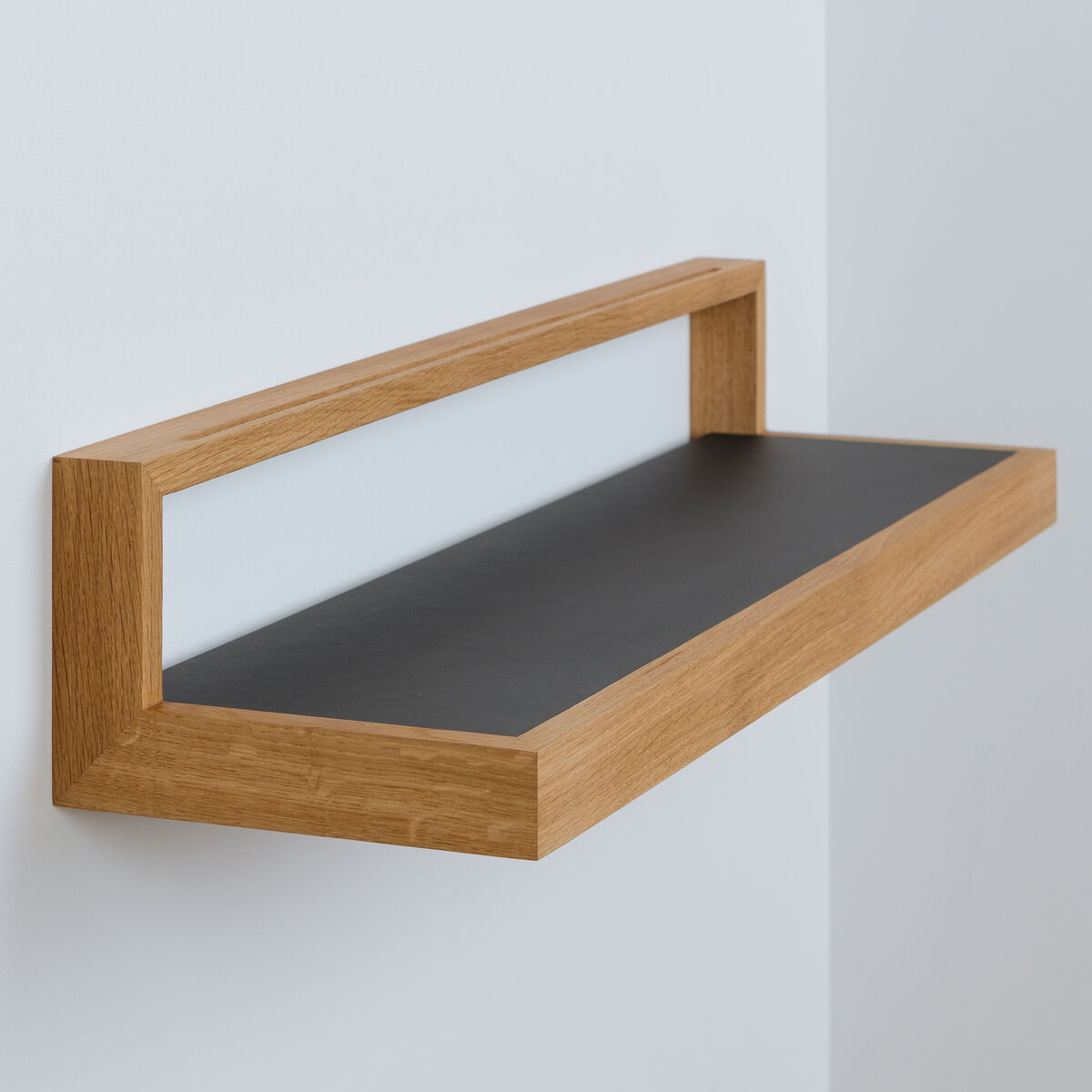 Das Bild zeigt das Ablagebord »buck« Größe 2 von das kleine b. Es besteht aus geölter Eiche mit einer anthrazitfarbenen Ablagefläche und aluminiumverstärkter Wandbefestigung. Die klare, minimalistische Form passt zu modernen, skandinavischen Einrichtungsstilen.