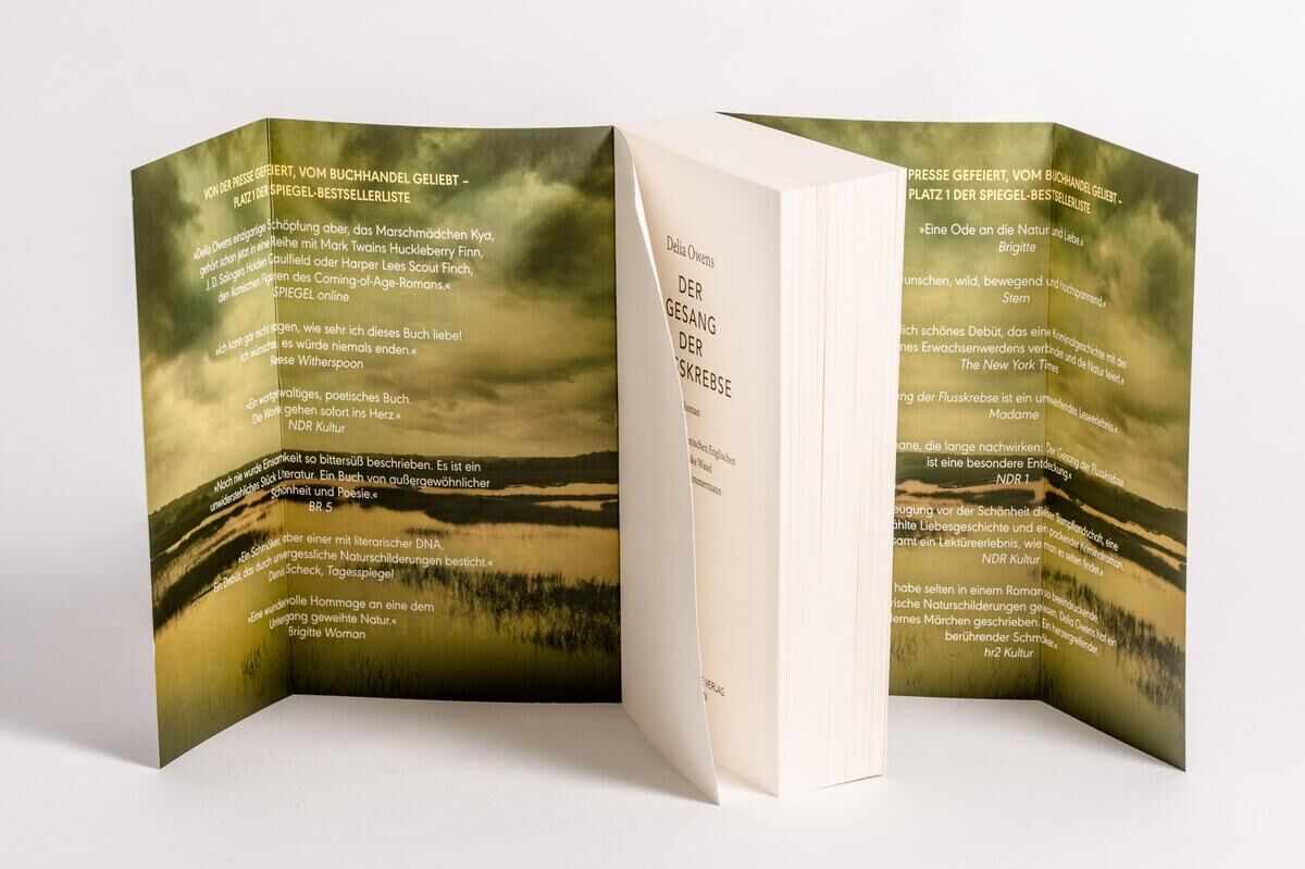Das Bild zeigt das Buch 'Der Gesang der Flusskrebse' von Delia Owens. Es ist aufgeklappt, und man sieht Text auf den inneren Seiten des Covers. Im Hintergrund ist eine Landschaft mit einem düsteren Himmel und einer sumpfigen Gegend abgebildet.