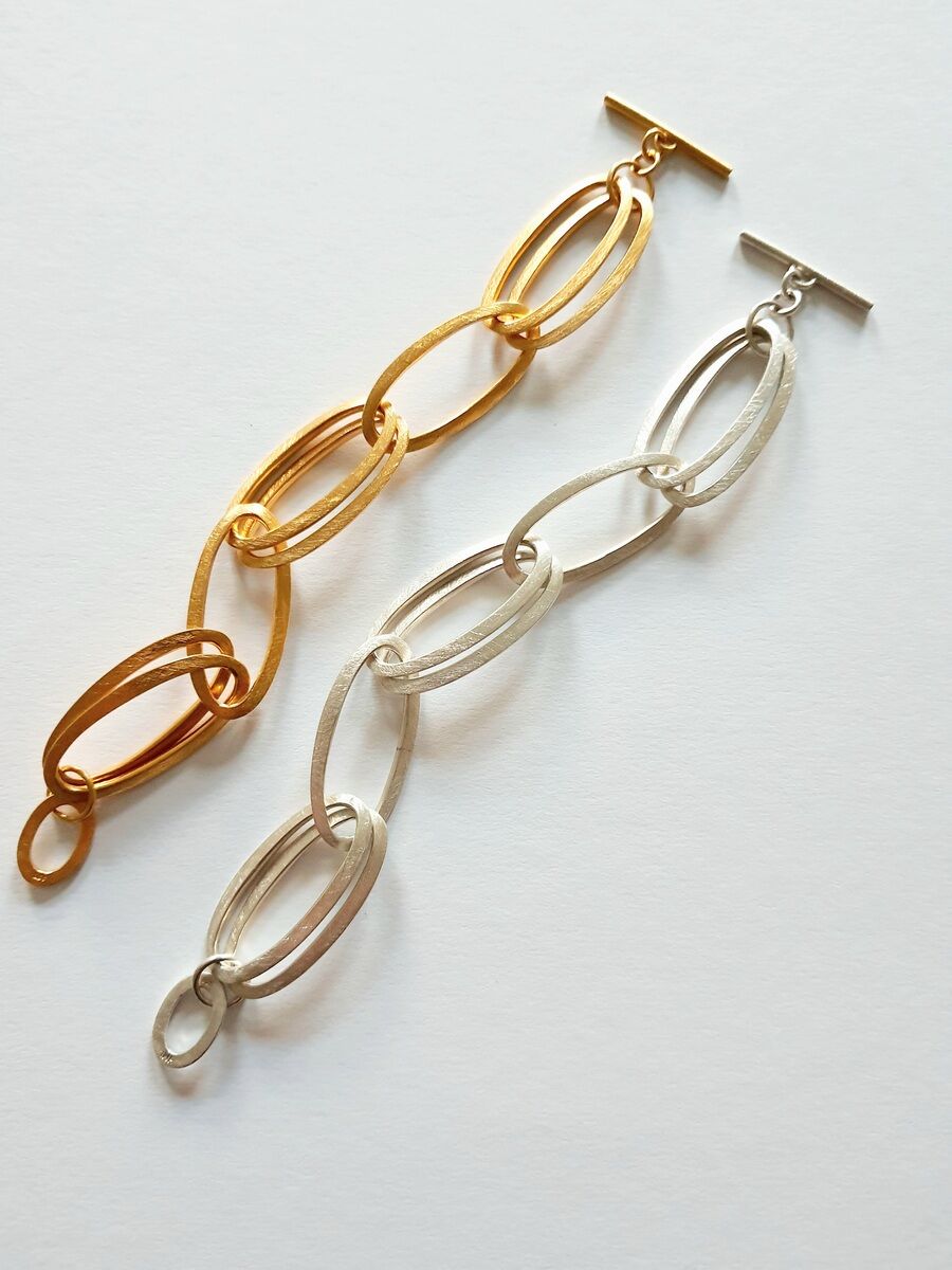 Zwei HML-Armbänder »GRACE« auf einer weißen Oberfläche. Ein Armband ist goldfarben, das andere silberfarben, beide bestehen aus ineinandergreifenden ovalen Gliedern.