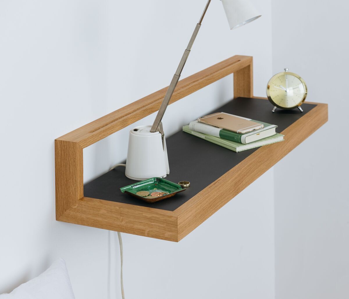 Ein modernes Wandregal mit Holzrahmen und anthrazitfarbener Platte, dekoriert mit Büchern, einer Lampe, einem Notizbuch und einer Uhr.