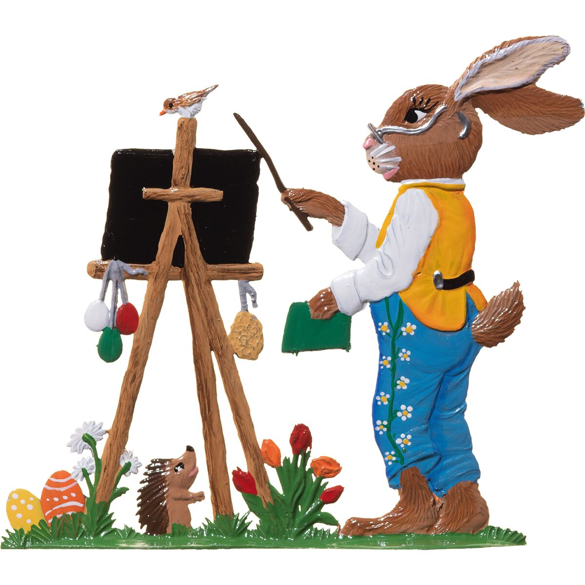 Detaillierte Zinnfigur eines stehenden Hasen in blauer Hose und gelber Weste, der mit einem Zeigestock an eine schwarze Tafel zeigt. Die Tafel steht auf einer Staffelei, darunter bunte Ostereier und Blumen. Ein Vogel sitzt auf der Staffelei, daneben ein Igel.