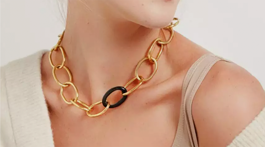 Frau trägt eine goldfarbene Gliederkette mit einem schwarzen Glied, sichtbarer Hals und Schulterbereich