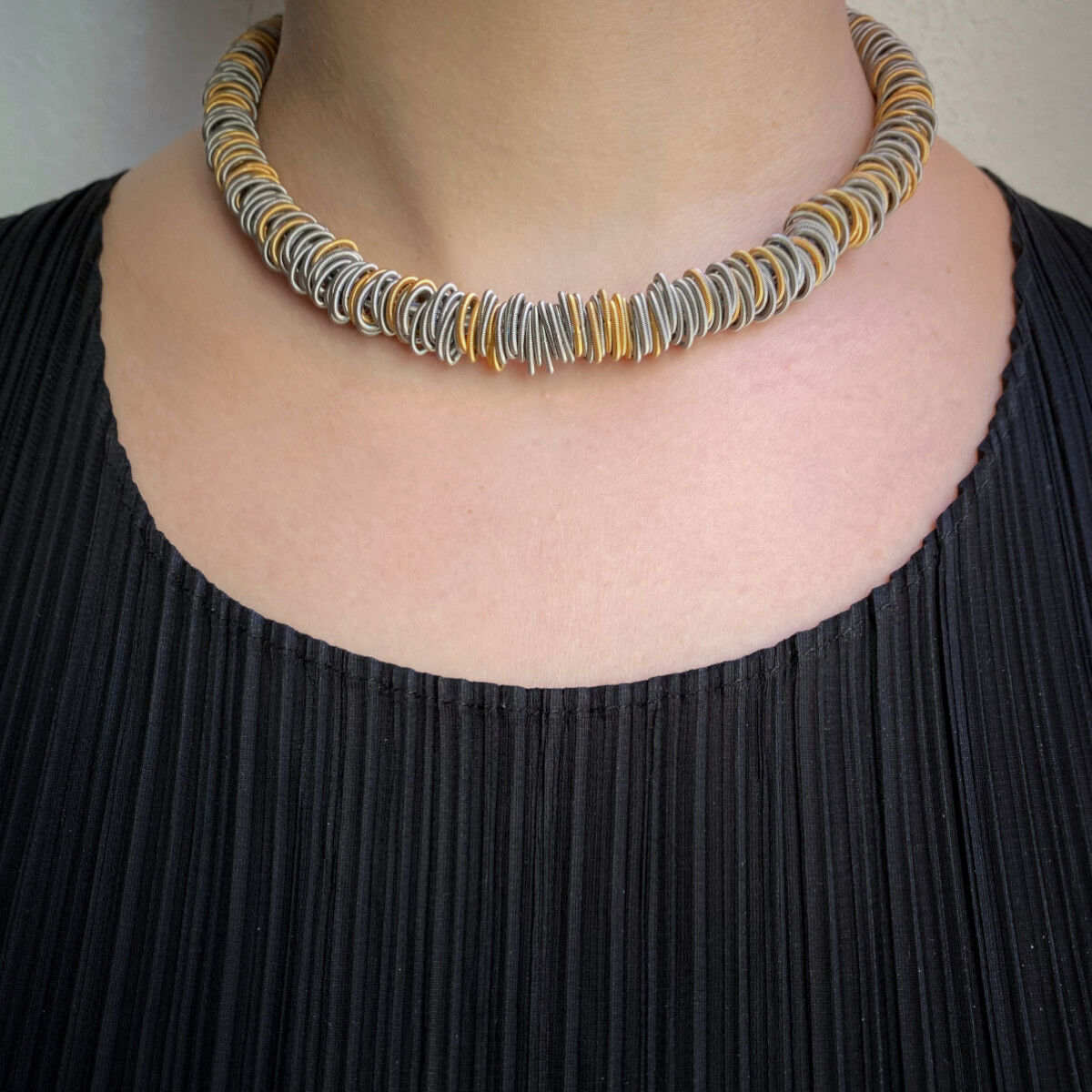 Eine Nahaufnahme einer eleganten Halskette, das »N°1 Collier«, getragen von einer Person mit schwarzem Oberteil. Das Collier besteht aus einer Vielzahl von silbernen und goldenen Elementen in einem modernen Design.