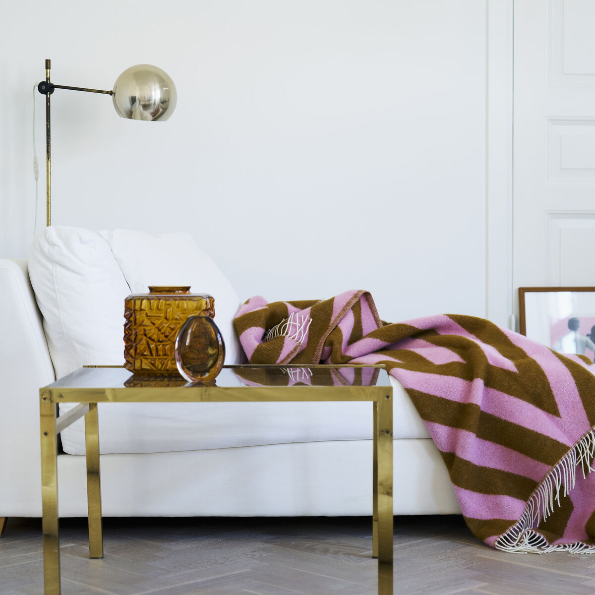 Eine braun-rosa gestreifte Decke namens »Tangent« liegt dekorativ auf einem weißen Sofa in einem modern eingerichteten Wohnzimmer mit goldenen Akzenten und stilvollen Accessoires.