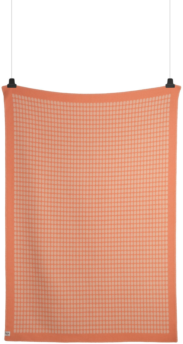 Eine orangefarbene Lammwolldecke mit Karomuster, die gerade an zwei Clips aufgehängt ist. Die Decke hat ein einfaches und elegantes Design, perfekt für gemütliche Herbst- und Winterabende.