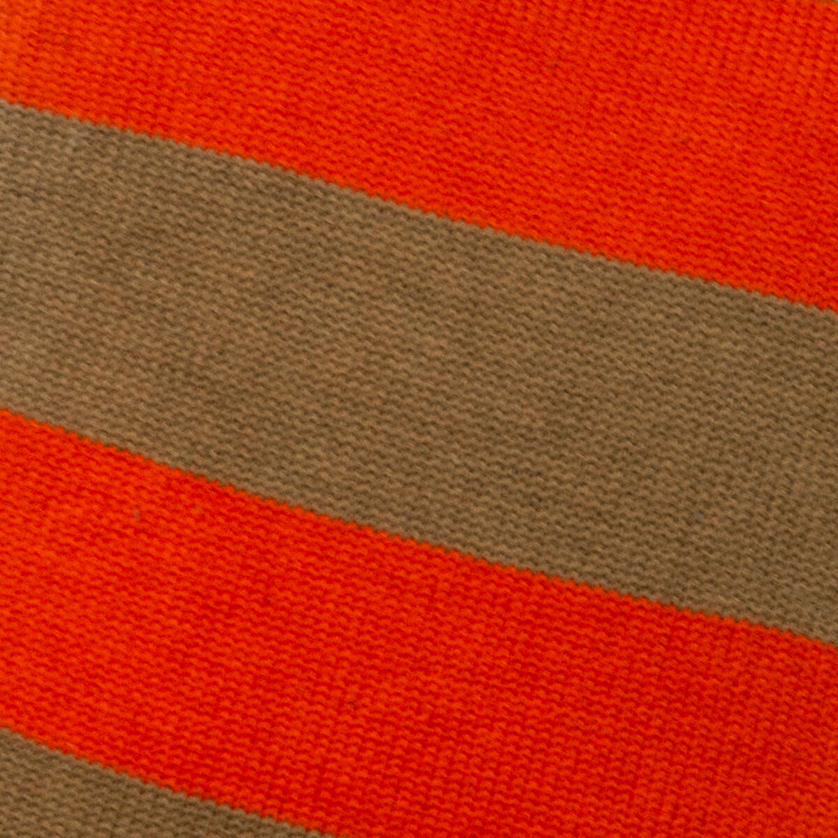 Nahaufnahme eines gestrickten Stoffes in kräftigen Streifen aus leuchtendem Rot und warmem Kamelbraun. Das Material besteht aus 100% Baumwolle und Latex. Es handelt sich um den Bezug einer Wärmflasche der Marke SUITE702, der weich und hochwertig verarbeitet ist.