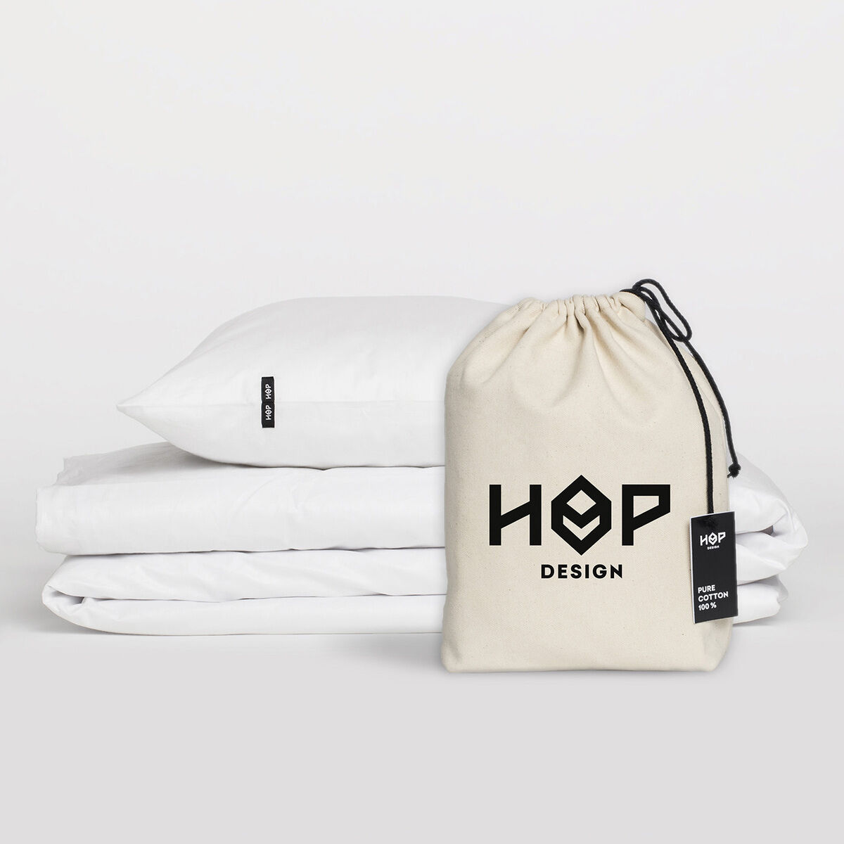 Ein Set Bettwäsche »Pure« von Hop Design, bestehend aus einem Kissen und einer Bettdecke in weißer Farbe, mit einem beigefarbenen Aufbewahrungsbeutel. Perfekt für ein modernes und schlichtes Schlafzimmer-Design.