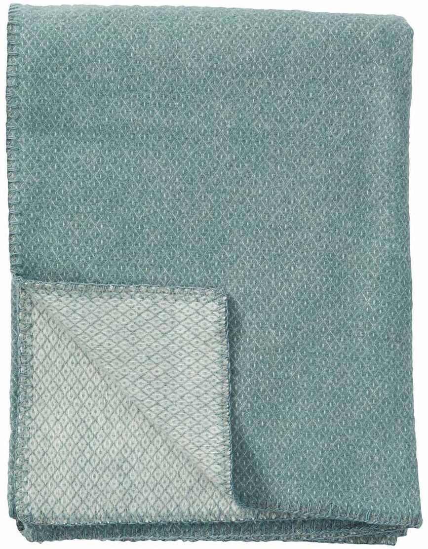 Decke »Peak« in Grün und Beige, gefaltet und teilweise aufgedeckt. Weiches Material mit texturierter Oberfläche.