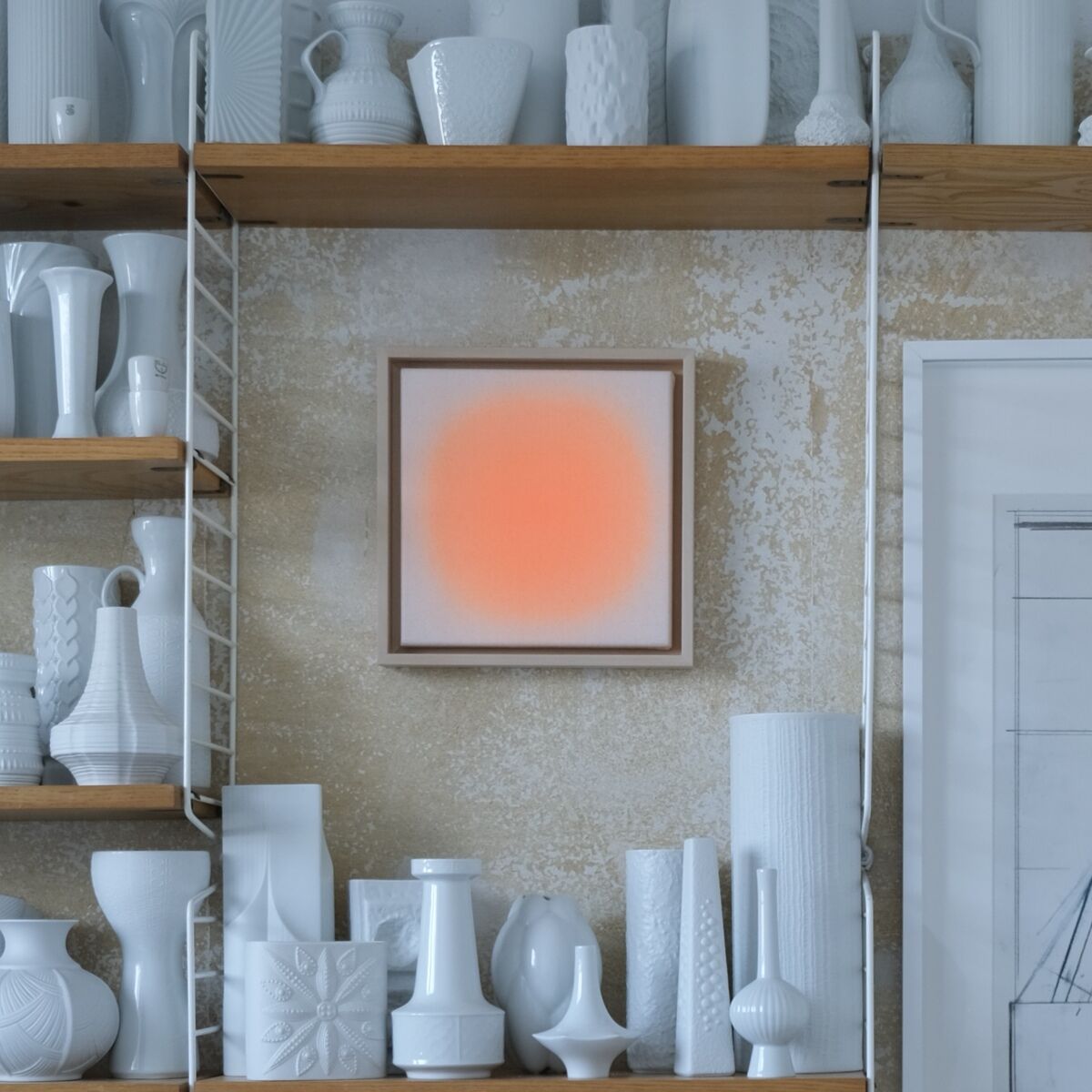 Stilvolle Wand mit offenen Holzregalen, darauf zahlreiche weiße Keramikvasen und Gefäße. Zentral ein Kunstwerk der ZEIT-Sonderedition »Sorbet« von Anastasia Benko: ein Unikat mit zartem, leuchtendem Orange auf beigem Grund, daneben ein großformatiger monochromer Kunstdruck.