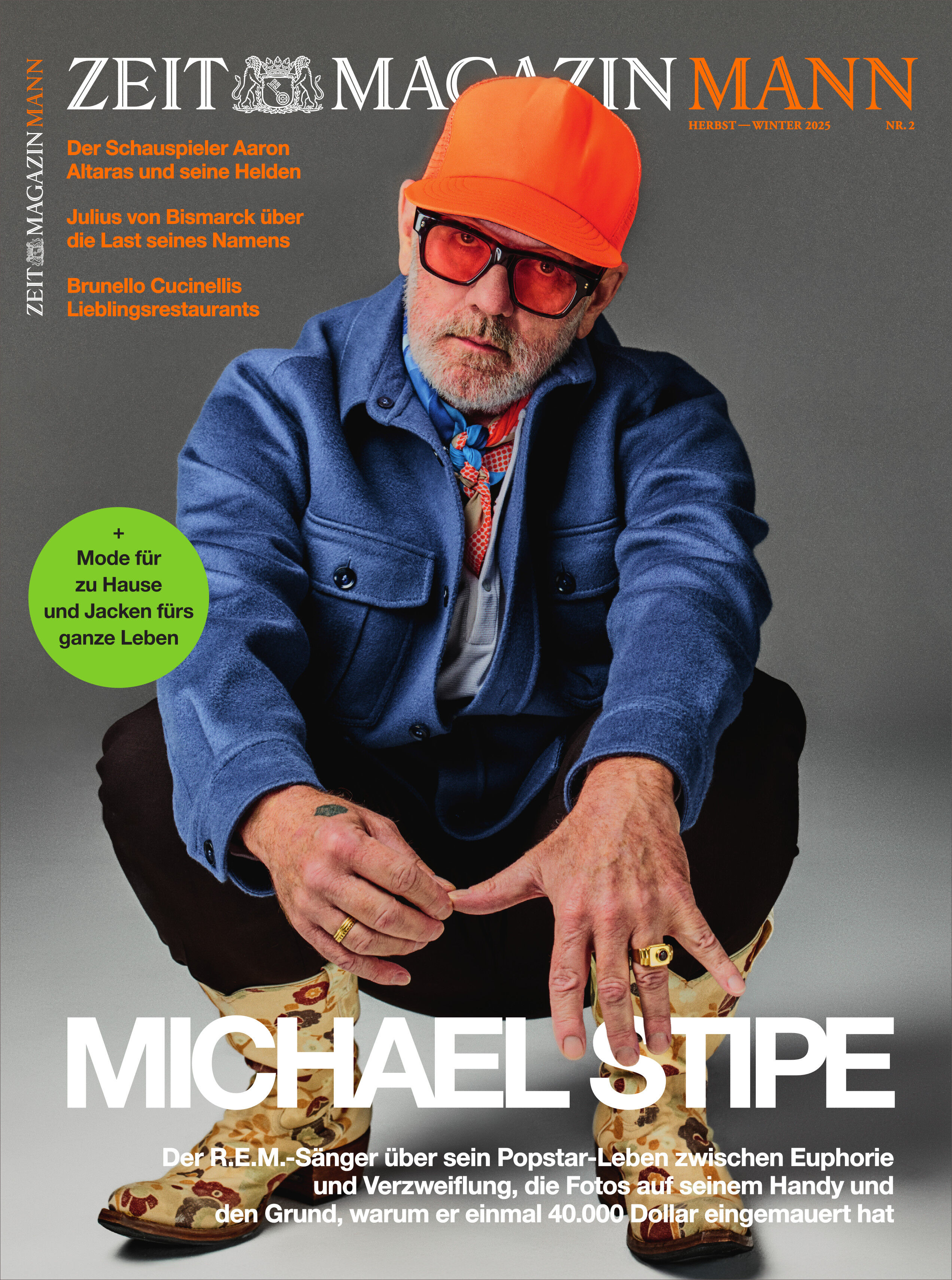 Titelbild des ZEITmagazin MANN 2/25 mit Michael Stipe; er sitzt auf dem Boden in einer modernen Pose und trägt eine blaue Jacke, eine orangefarbene Kappe, runde Brille und gemusterte Schuhe vor grauem Hintergrund. Das Cover zeigt zudem Textinfos und einen grünen Kreis mit Mode-Tipp.