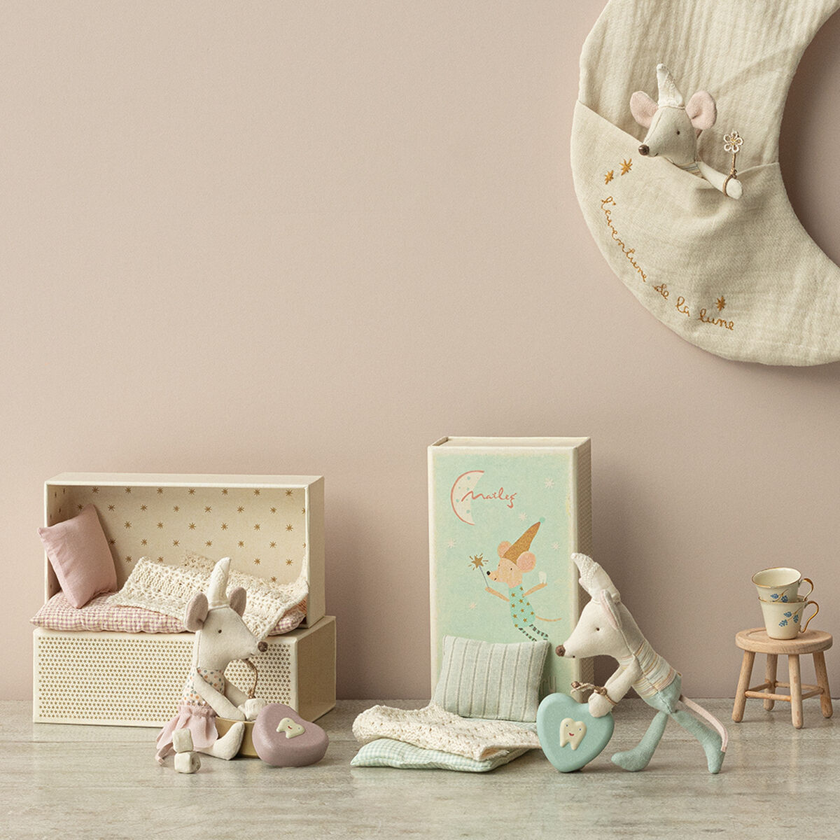 Detailaufnahme eines Kinderzimmer-Sets, einschließlich einer Zahnfeemaus aus Stoff, die auf einer kleinen Holzmöbelanordnung präsentiert wird. Beige, rosa und blaue Töne dominieren das Bild, mit einer dekorativen Umrandung, die einen freundlichen und gemütlichen Eindruck hinterlässt.