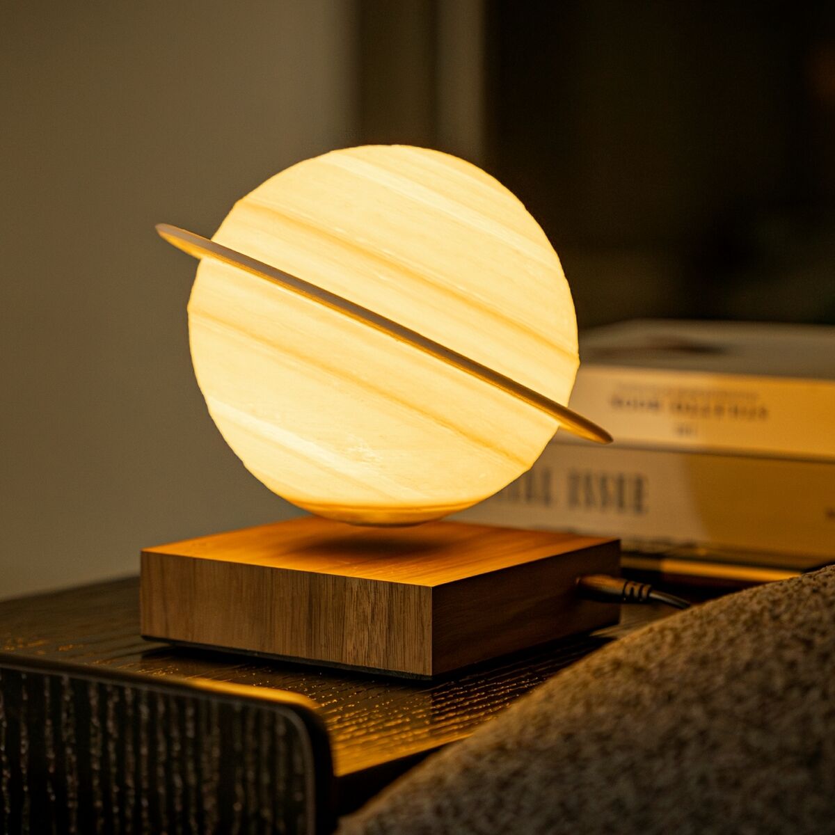 Eine moderne Tischlampe in Form des Planeten Saturn mit warmem Licht auf einem Holzsockel, geeignet für stimmungsvolle Beleuchtung und dekorative Zwecke.