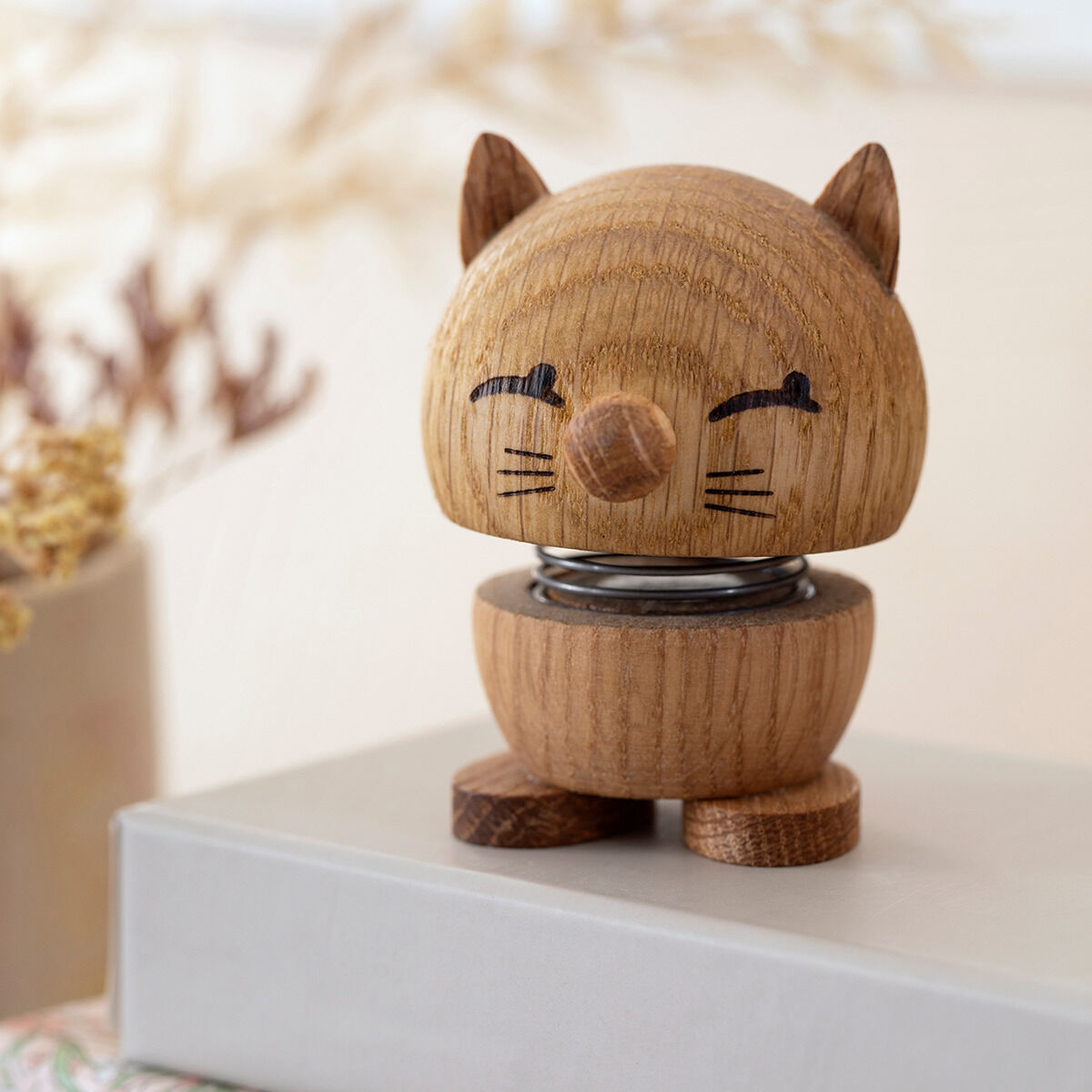 Holzfigur in Katzengestalt aus Eiche von Hoptimist, auf einem Tisch platziert, mit minimalistischem Design und fröhlichem Ausdruck.