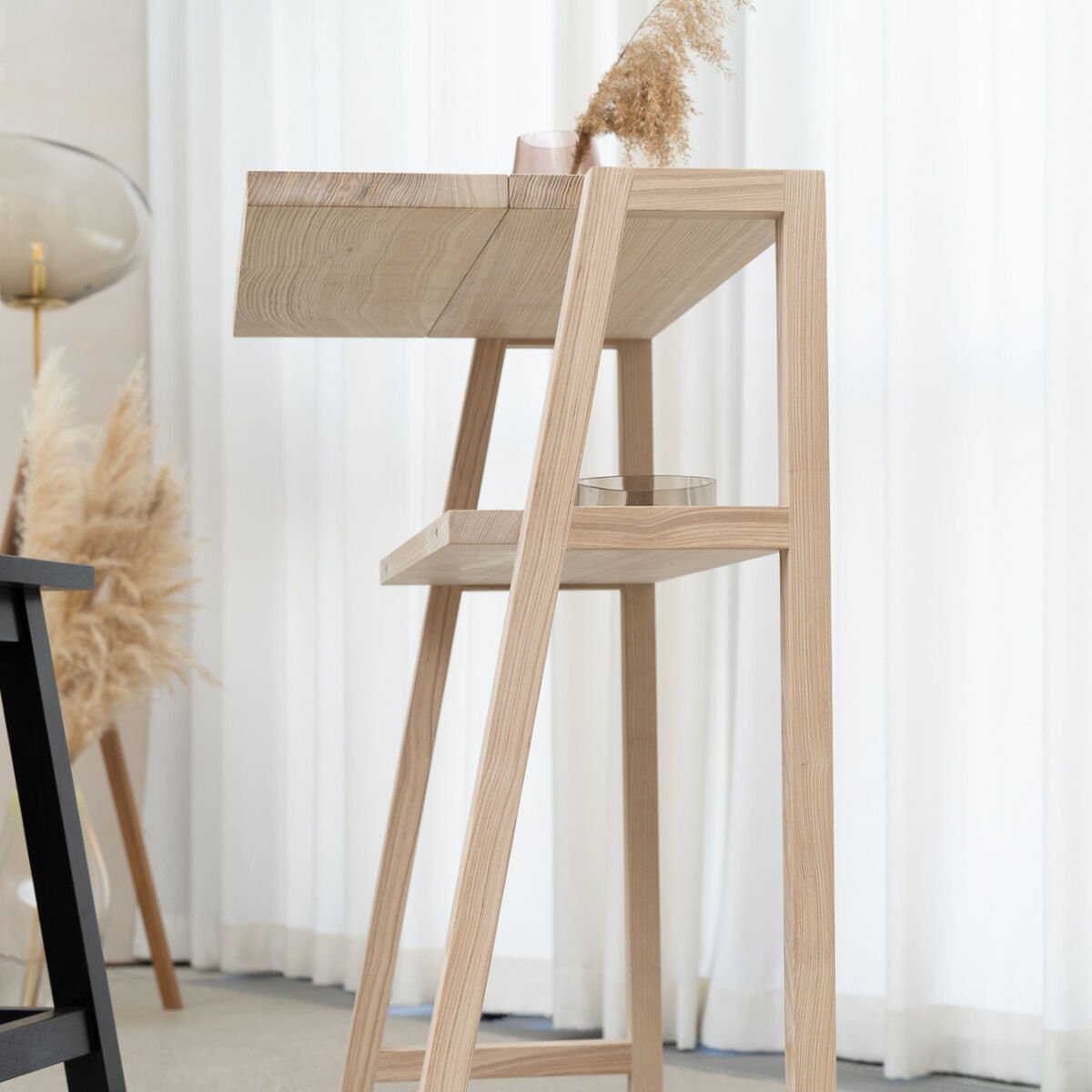 Das Bild zeigt das KultPult "SCALA" von Frau Caze, ein Stehpult aus hellem Holz mit klaren, modernen Linien. Im Hintergrund helle Vorhänge und dekorative Elemente aus Pampasgras, das Gesamtbild ist minimalistisch und freundlich gehalten.