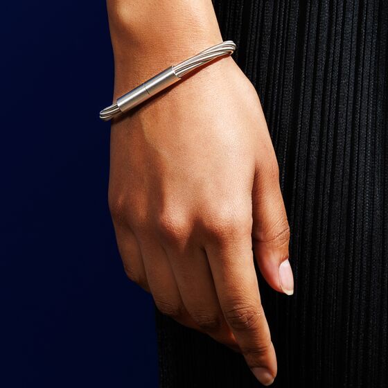 Nahaufnahme eines modernen Armbands in Kabel-Optik aus silberfarbenem Metall, getragen am Handgelenk vor dunklem Hintergrund.