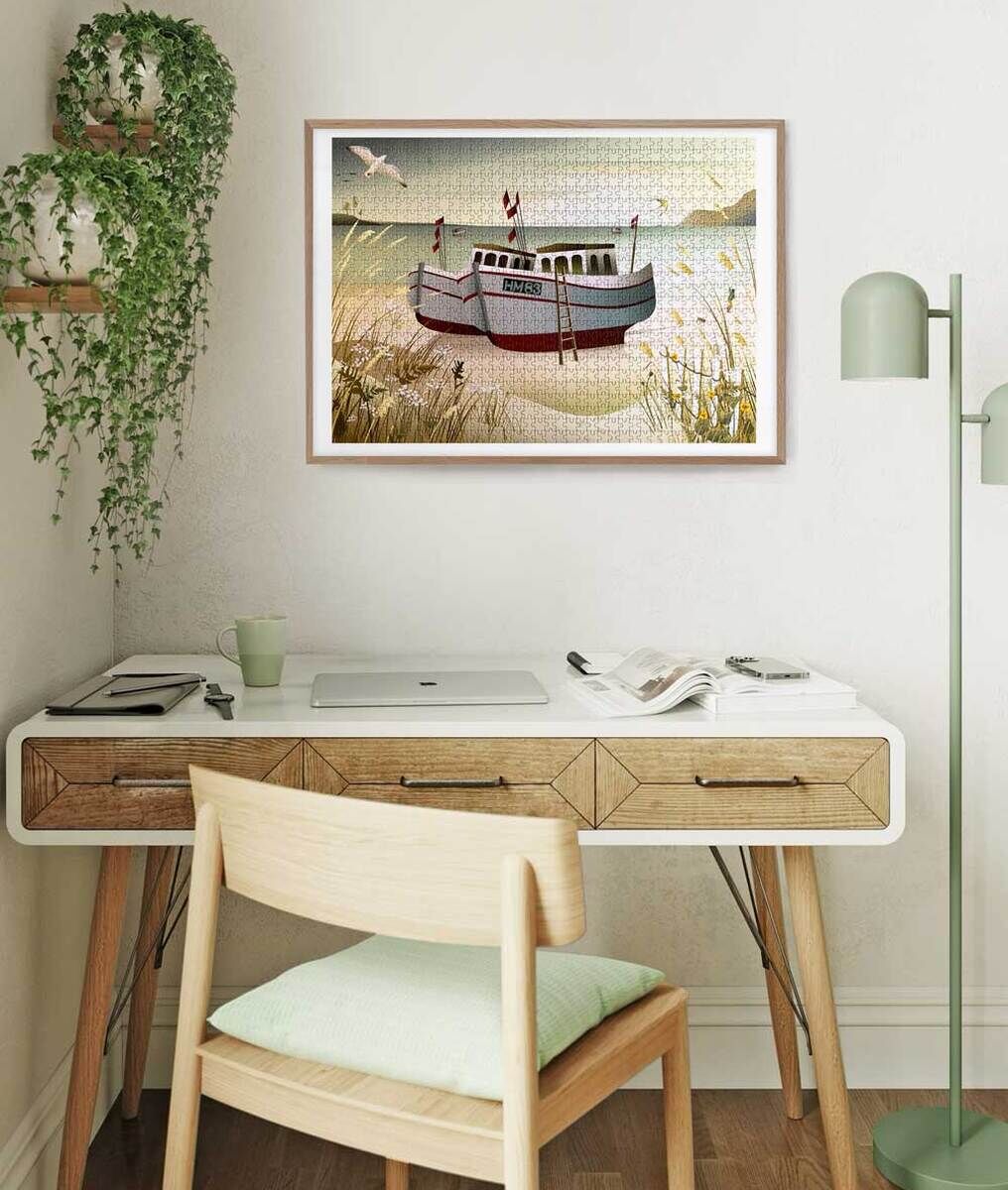 Ein dekoriertes Wohnzimmer mit einem Wandpuzzle, das ein Fischerboot an einer Küste zeigt. Der Raum ist schlicht gestaltet mit einem Holztisch, einem Stuhl und einer Stehlampe. Pflanzen und neutrale Töne dominieren das Ambiente.
