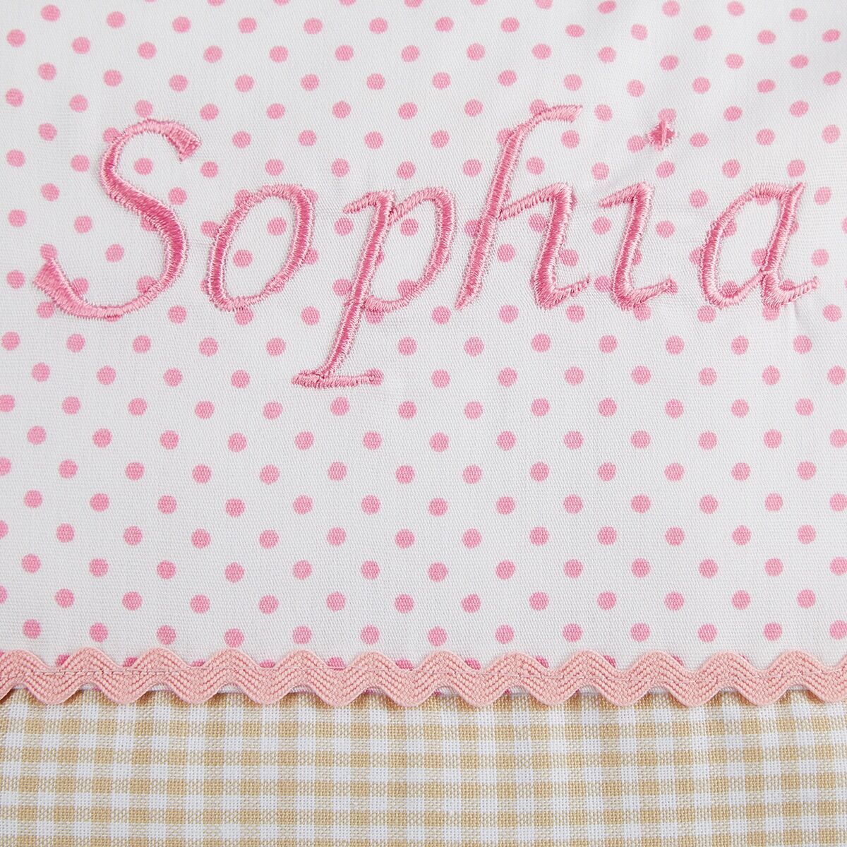 Ein personalisiertes Namenskissen mit dem Namen 'Sophia'. Das Kissen hat ein Design mit rosa Punkten, zackigen rosa Borten und einem unteren Abschnitt mit gelb-weißem Karomuster.