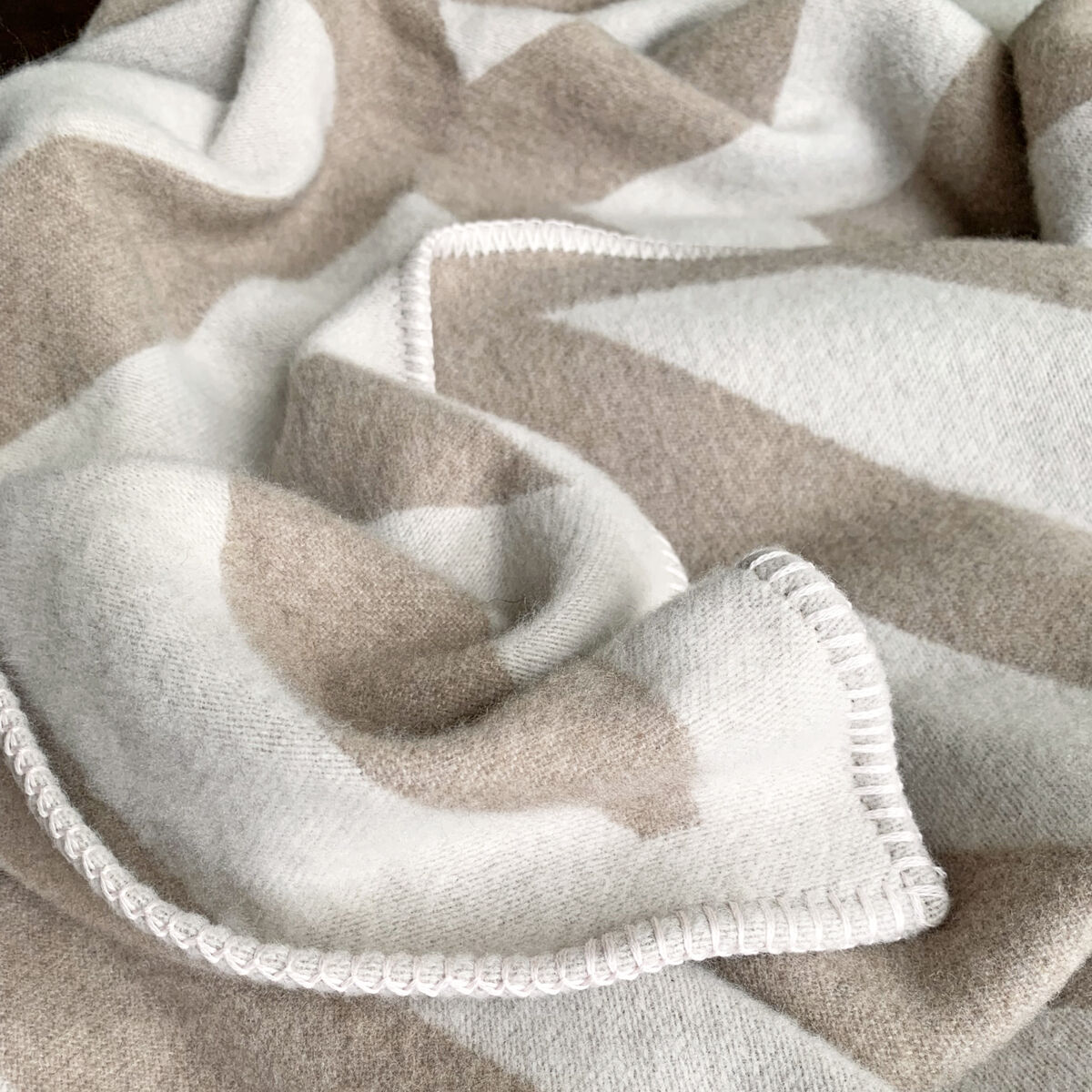 Kaschmirdecke »Pontresina« mit braun-weißem geometrischem Muster liegt gefaltet. Die Decke hat eine weiche Textur und hochwertige Verarbeitung.