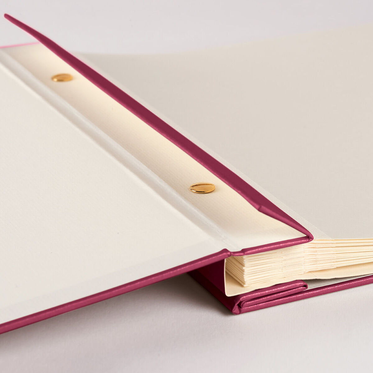 Ein aufgeklapptes Fotoalbum zeigt eine weiße und rosa Innenseite mit goldenen Halterungen. Die Seiten des Albums sind beige.
