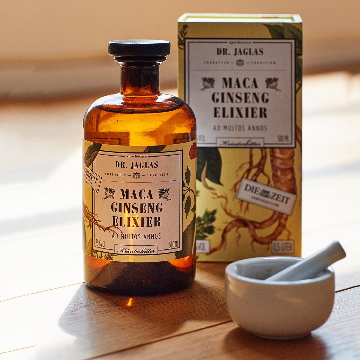 Eine Flasche ZEIT-Sonderedition »Maca Ginseng-Elixier« von Dr. Jaglas neben ihrer Verpackung auf einem Holzuntergrund. Neben der Flasche steht ein weißer Mörser mit Stößel.