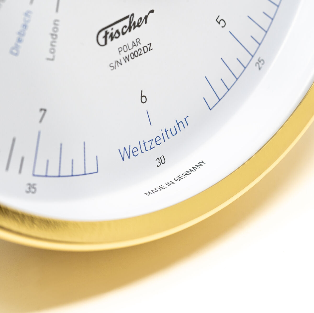 Nahaufnahme einer Weltzeituhr der ZEIT-Sonderedition »POLAR Weltzeituhr« von Fischer Manufaktur mit goldenem Rahmen und weißem Zifferblatt. Die Uhr zeigt Städtenamen und eine präzise Sekundenskala. Hergestellt in Deutschland.