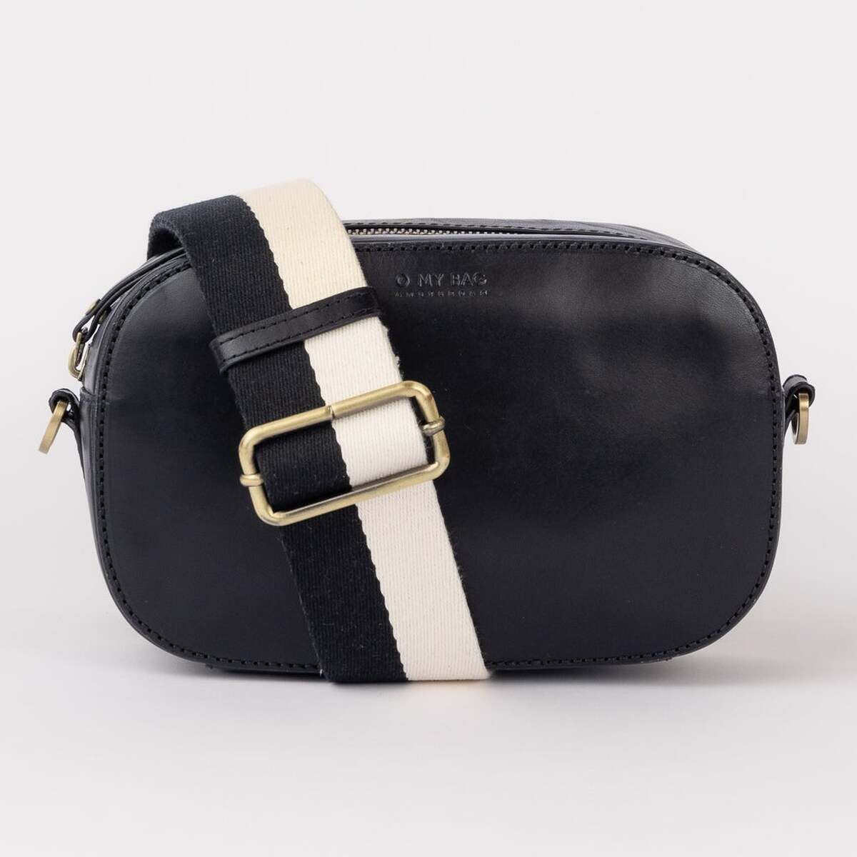Eine kleine, moderne Umhängetasche namens Maya mit abgerundeter Form, schwarzem Korpus und verstellbarem Schulterriemen in Schwarz und Weiß sowie goldfarbener Schnalle vor hellem Hintergrund. Die Tasche eignet sich ideal für den Alltag oder besondere Anlässe.