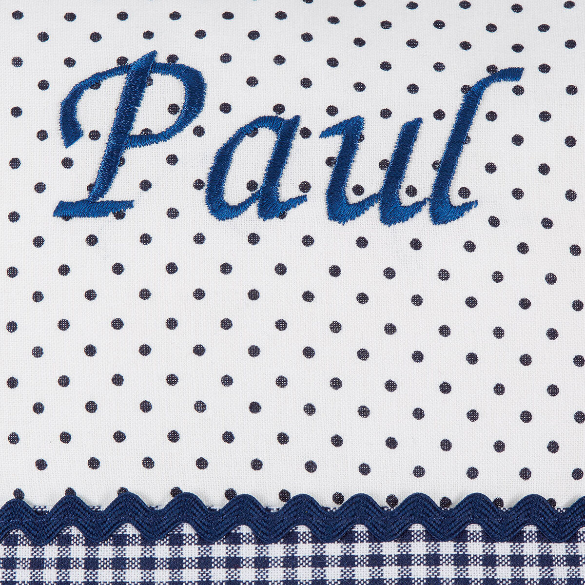 Namenskissen mit dem Schriftzug 'Paul' in blauer Stickerei auf weißem Stoff mit schwarzen Punkten und blau-weiß kariertem Rand.
