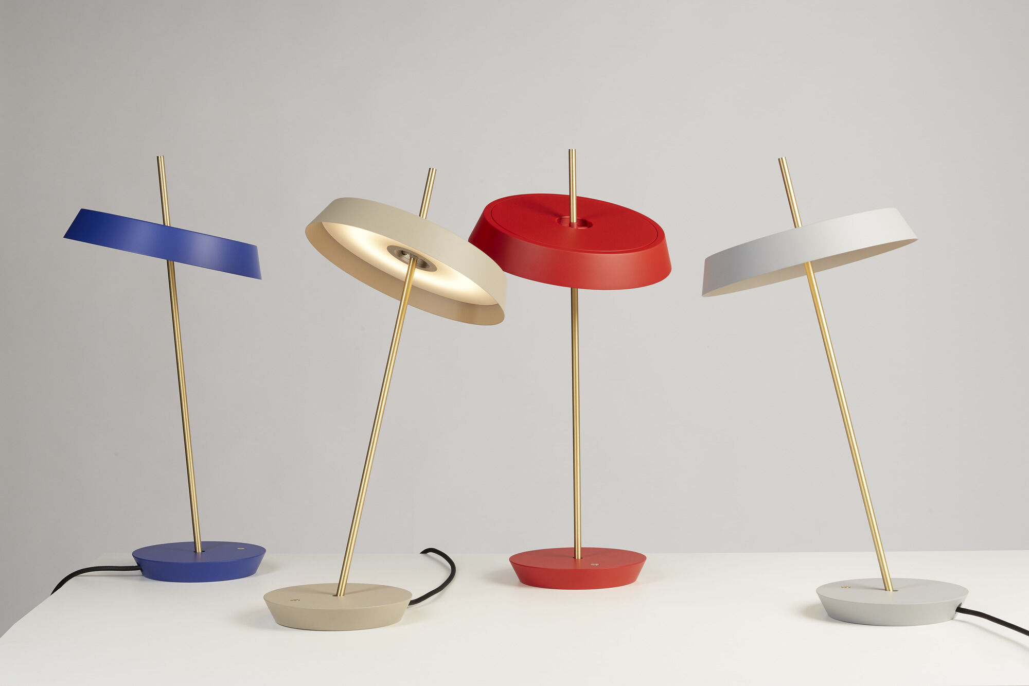 Vier moderne Stehlampen mit bunten Schirmen - rot, blau, weiß und beige - gepaart mit goldenen Stielen auf hellgrauem Hintergrund.