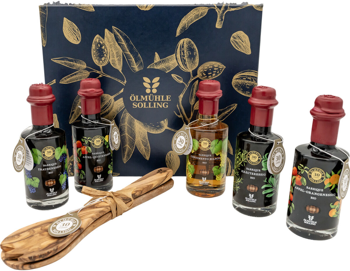 Edle Präsentbox von Ölmühle Solling mit fünf Jubiläumsessigen in dekorativen Flaschen, je mit rotem Wachssiegel und liebevoll gestalteten Etiketten, ergänzt durch ein hochwertiges Salatbesteck aus Holz. Die Box ist dunkelblau mit goldfarbenem Pflanzenmotiv und Logo.