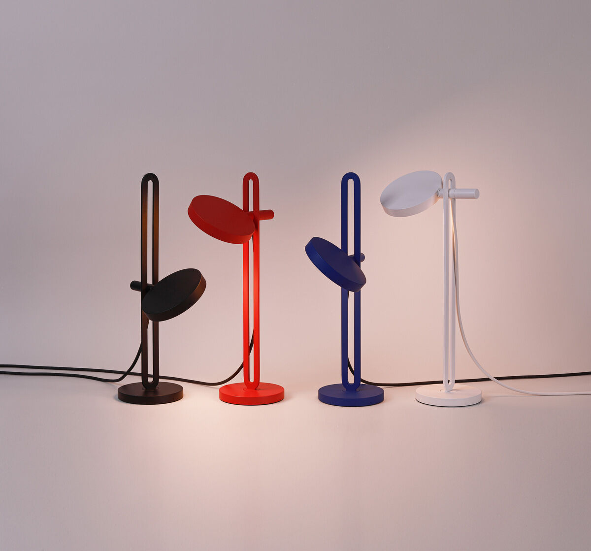 Eine Reihe von vier modernen Tischlampen der Marke »Echo« in den Farben Schwarz, Rot, Blau und Weiß, die nebeneinander auf einer Oberfläche stehen.