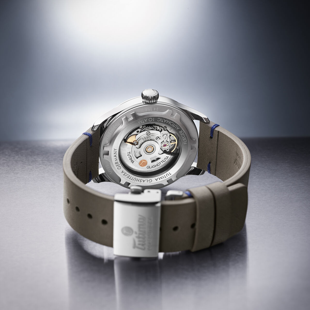 Die Rückseite der ZEIT Sonderedition »Flieger Aero Club« Automatikuhr zeigt ein transparentes Gehäuse, durch das das mechanische Uhrwerk sichtbar ist. Die Uhr hat ein graues Lederarmband und ein silbernes Metallgehäuse.