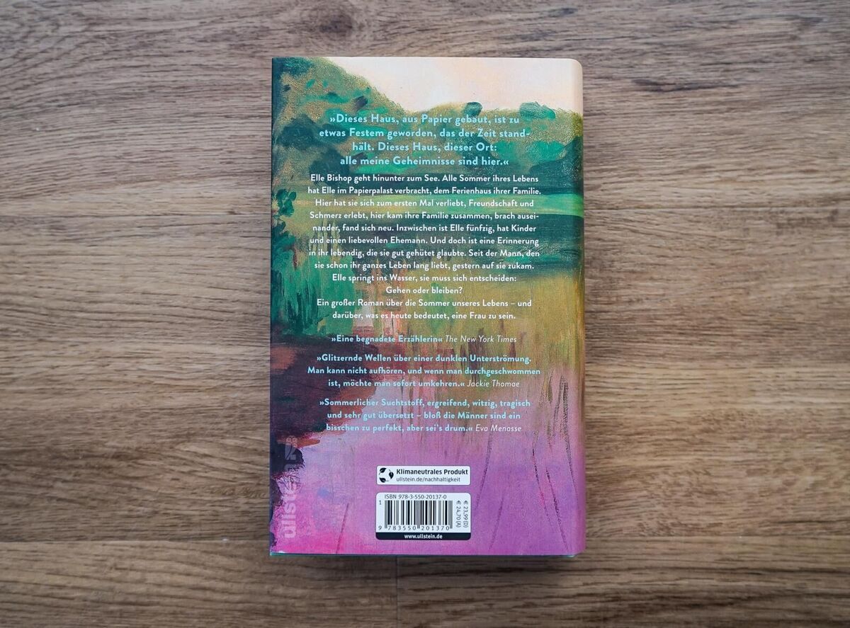 Die Rückseite des Buches 'Der Papierpalast' von Miranda Cowley Heller, liegend auf einem Holztisch. Der Buchrücken zeigt einen Farbmix aus Grün, Gelb, Pink, und Orange. Es ist Text auf dem Buchrücken sichtbar.